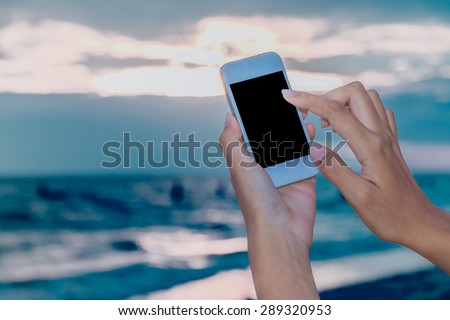Asian woman holding mobile (red case) on the beach background