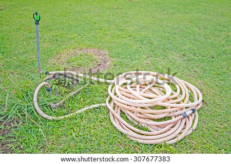 Reel of hose pipe and spraying head on grass with sprinkler