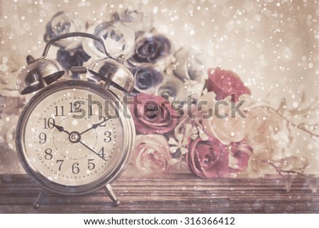 Vintage alarm clock on table.10.10 am with bokeh and rose flower on wood table