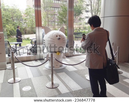 Tokyo, Japan - July 07, 2014: A Japanese businessman taking cellphone pictures of the official mascot for Toranomon Hills in the Toranomon Hills building.