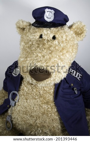 Oversized teddy bear dressed in police uniform with handcuffs and whistle.