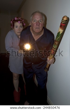 Older couple - man with a bat and woman with hair in curlers - aroused from bed in pajamas responding to noises at night.