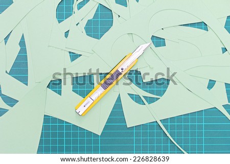 Box cutter yellow handle with scratches from use and paper being cut , Placed on the green cutting mat