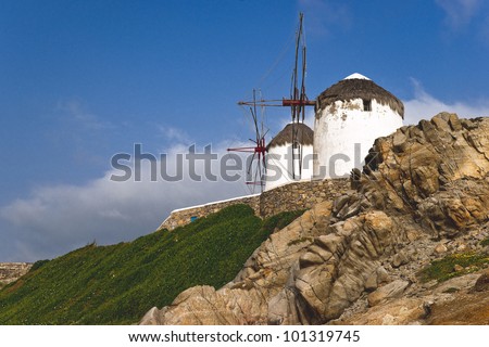 Two windmills of Mykonos town on the top of green grass mountainside