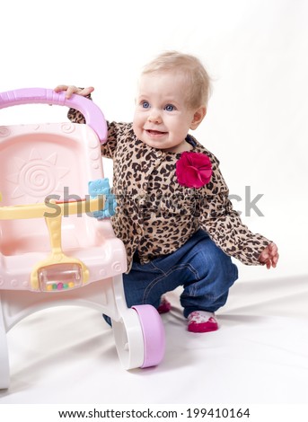 Beautiful baby kneeling down next to toy baby carriage. Shot in a studio. Isolated on white. Focus on face