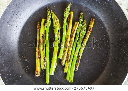 Green asparagus is cooked in frying pan.