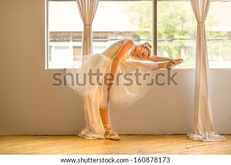teen girl ballet dancer stretching beside a window