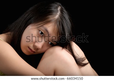 young attractive asian woman sitting on a black background with her head on her knees thinking