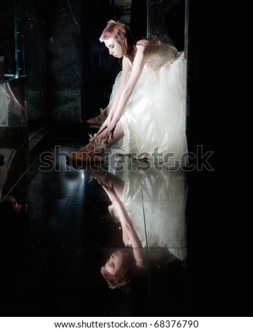 ballet dancer sitting in a tutu stretching on a black reflective background