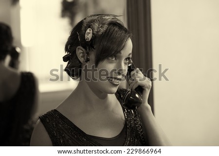 Sepia tone retro photo of a woman in a flapper dress and head dress talking on an old telephone.