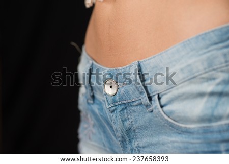 close up of the tummy torso of a young woman in jeans with belly exposed.