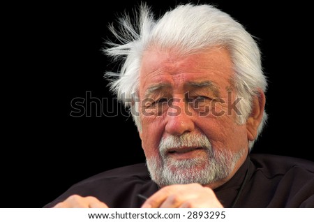 A mature gentleman with wind-blown silver hair, against a black background