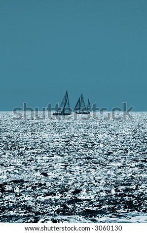Two sailboats passing on the Pacific Ocean at the end of the day