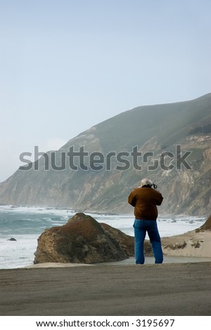 A mature gentleman making a photograph of the mouth of the Little Sur river.