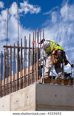 A construction worker guiding a section into place on a high concrete wall, shot against a cloudy sky.