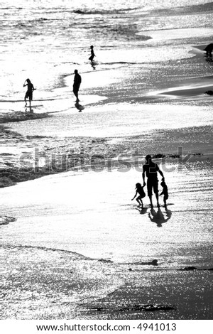 A black and white image of a father and his children playing in the surf at sunset