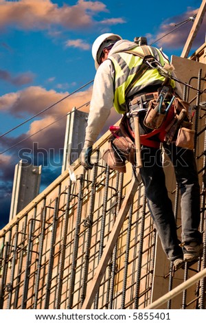 A construction worker on a high wall against colorful sunrise clouds.