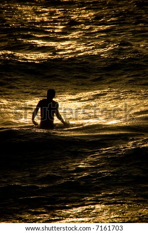 An image of a young man on Maui, standing in the Pacific Ocean, bathed by the golden light of the setting sun.