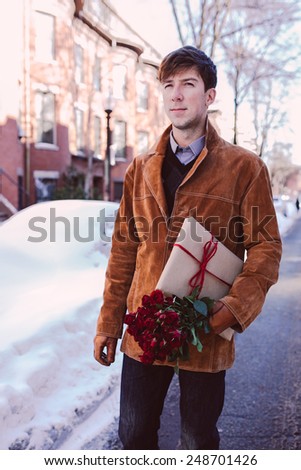 Young man with red roses and a present walking on a winter background