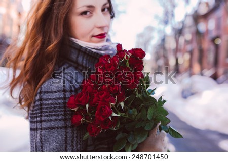 Young woman admiring red roses on a winter background