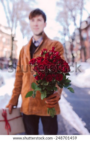 Young man with red roses and a present walking on a winter background