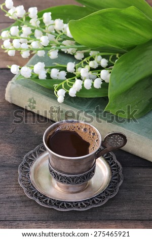 A cup of hot coffee, a bouquet of lilies of the valley, the old book