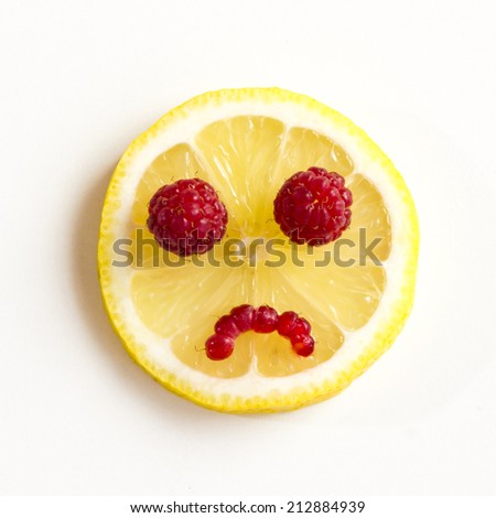 Sad eyes of lemon with raspberries on a white background.