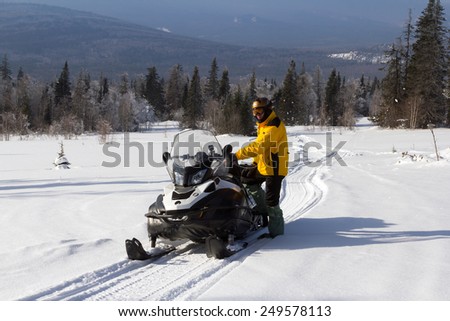 The athlete stands near the snowmobile in the winter in the mountains of the Southern Urals.
