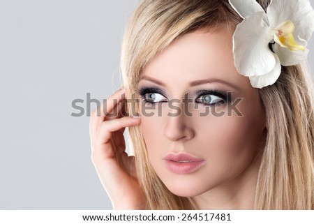 Closeup Beauty Female Face Spa. Beautiful Young Woman Model with White Flower Orchid in Her Blonde Hair touching Cheek.