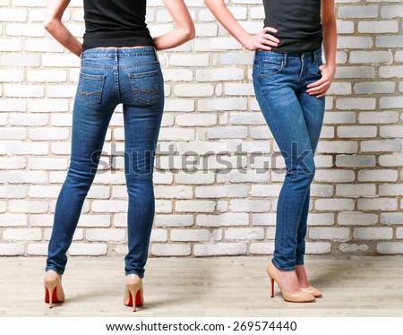 Close up Female Legs in Jeans on brick wall background. Slim Woman Wearing Blue Skinny Jeans. Back and Side View.