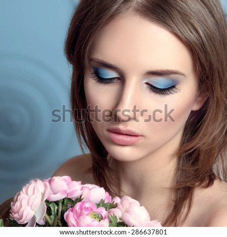 Portrait of beautiful natural looking young woman model with fresh daily makeup and romantic flower bouquet. Perfect clear skin, sexy gloss lips, blue eyes make up and long lashes. Makeup.