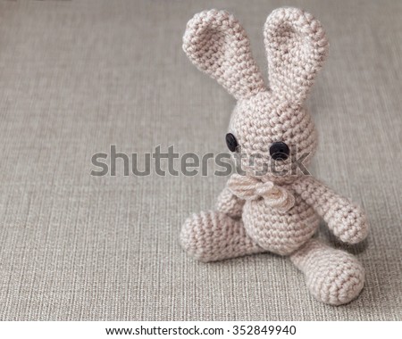 Handmade crochet rabbit toy on burlap rustic background. Amigurumi doll, space for text