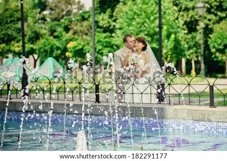 happy bride and groom standing near the fountain in the park