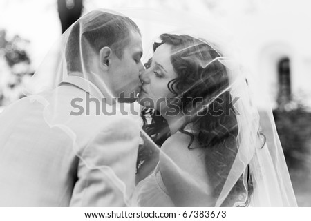 black and white portrait of the bride and groom kissing behind veil