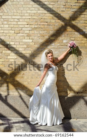 a bride in a wedding dress stands near the brick wall