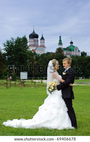 bride and groom standing in the park against the backdrop of the church
