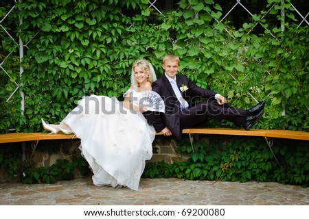 happy bride and groom sit on the bench back to back