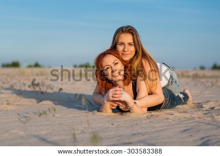 Two beautiful women laying together on sand outdoor