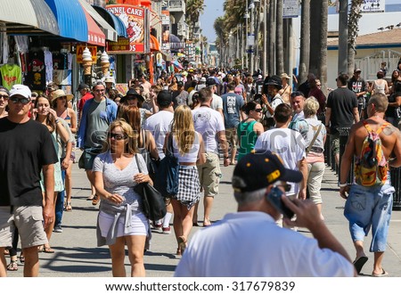 VENICE BEACH, USA - JUNE 4, 2014: The crowded Venice Beach Boardwalk. Lots of people are strolling down the boardwalk. On the sides there are several shops and palm trees.