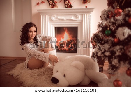 Beautiful young girl sitting beside the fireplace and Christmas tree