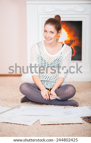 Young girl with blank whatman for drawing and with colored pencils on the floor