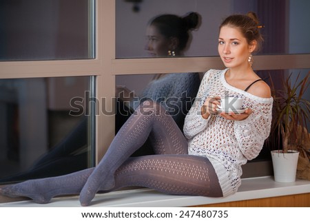 Portrait of a happy young woman relaxing at home with cup of tea on the window sill