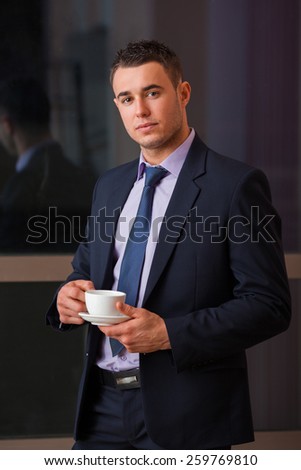 Portrait of a handsome guy in suit holding coffee cup indoor.