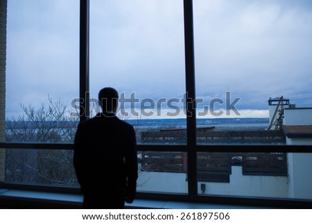 Businessman thinking in office, looking out of windows to downtown
