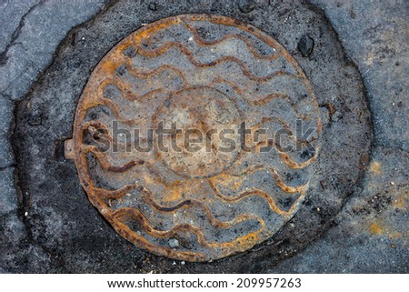 Manhole with rusty metal cover in cracked asphalt surface