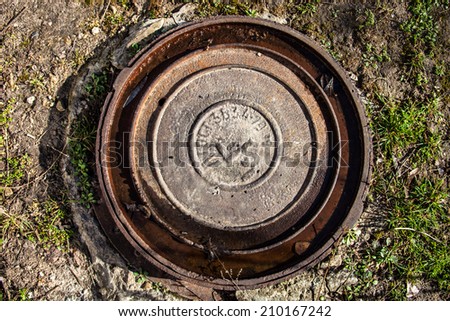 Manhole with rusty metal cover and water in its grooves