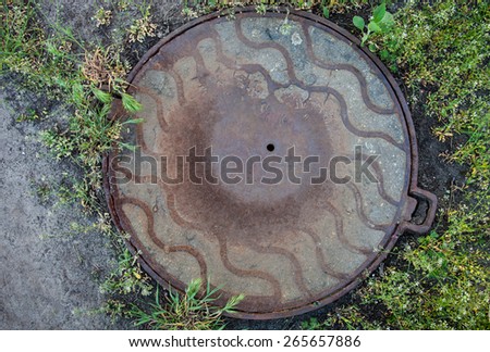 Manhole with rusty metal cover in the green grass