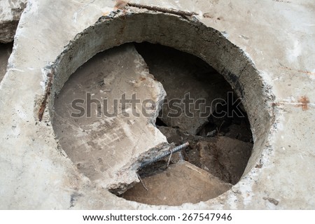 Concrete block with the manhole opening on the pile of damaged concrete blocks.