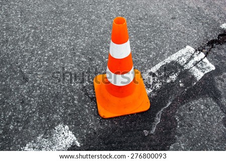 Traffic cone on the asphalt surface with partly rubbed out white road marking line. Close up.