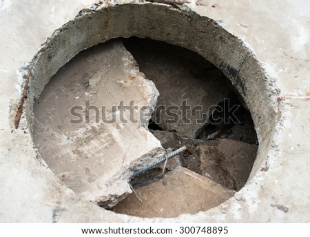 Concrete block with the manhole opening on the pile of damaged concrete blocks.